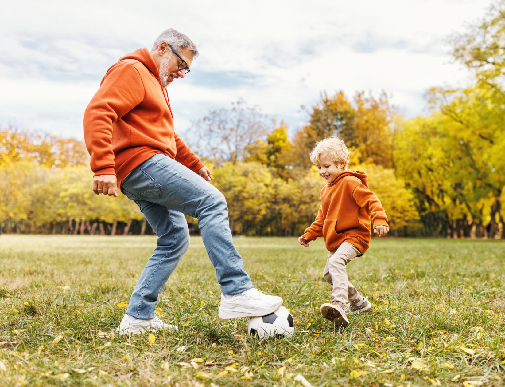 Happy family grandfather and grandson play football on lawn in park